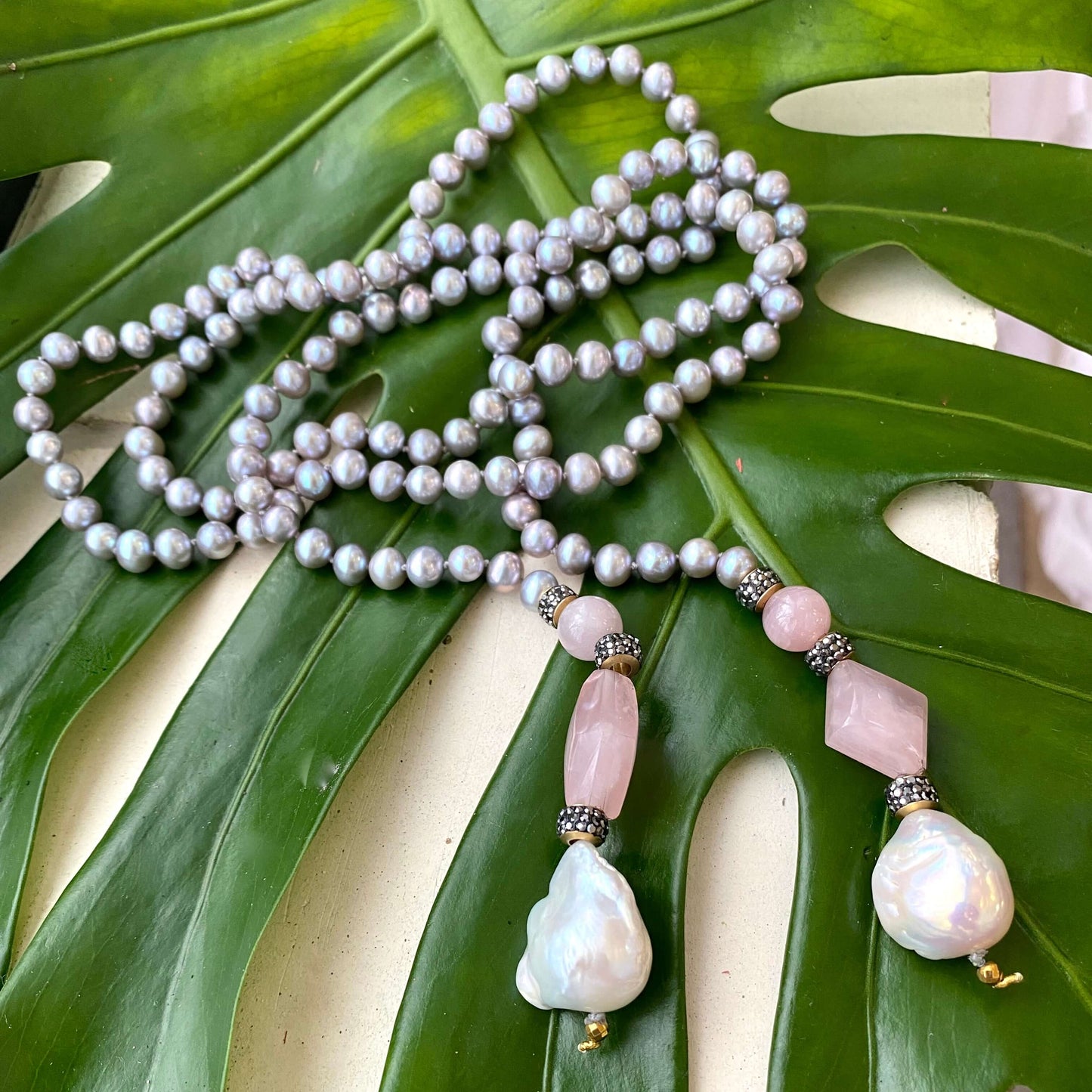 Pastel pearl lariat necklace featuring blue-gray freshwater pearls and pink rose quartz on a green leaf background.