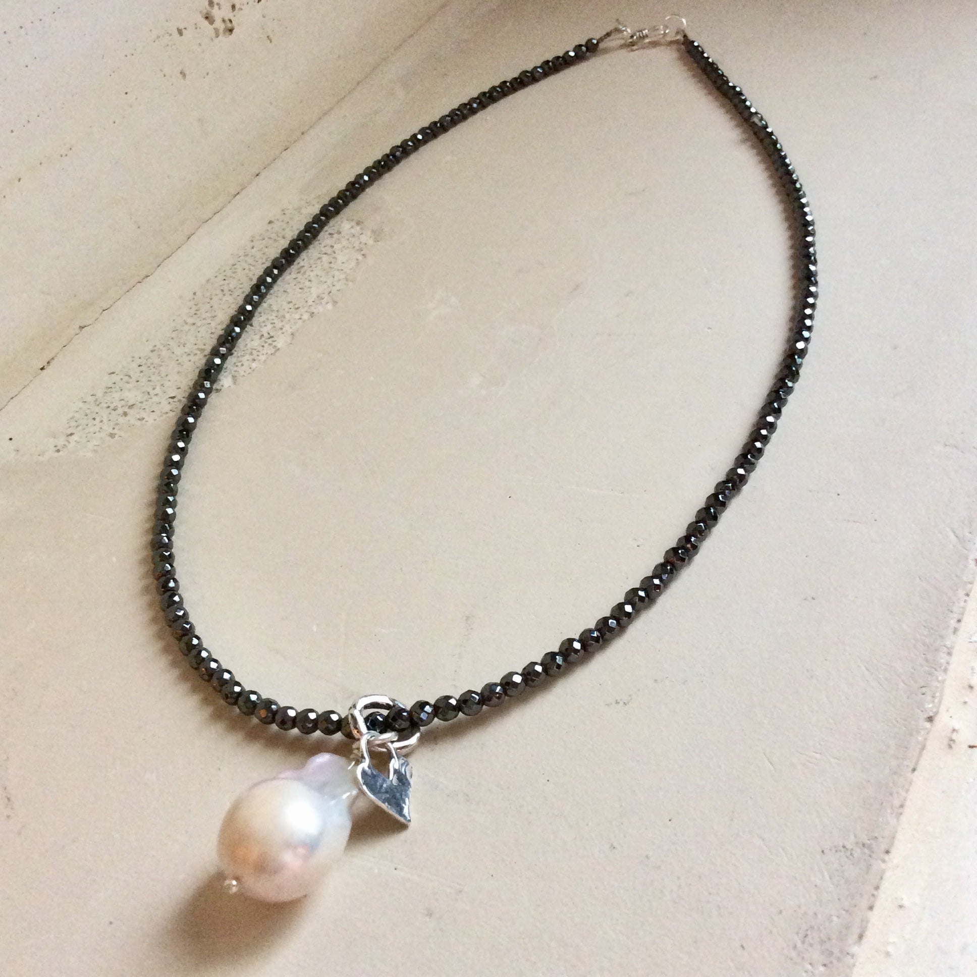 Hematite necklace with baroque pearl pendant displayed flat emphasizing minimalist design