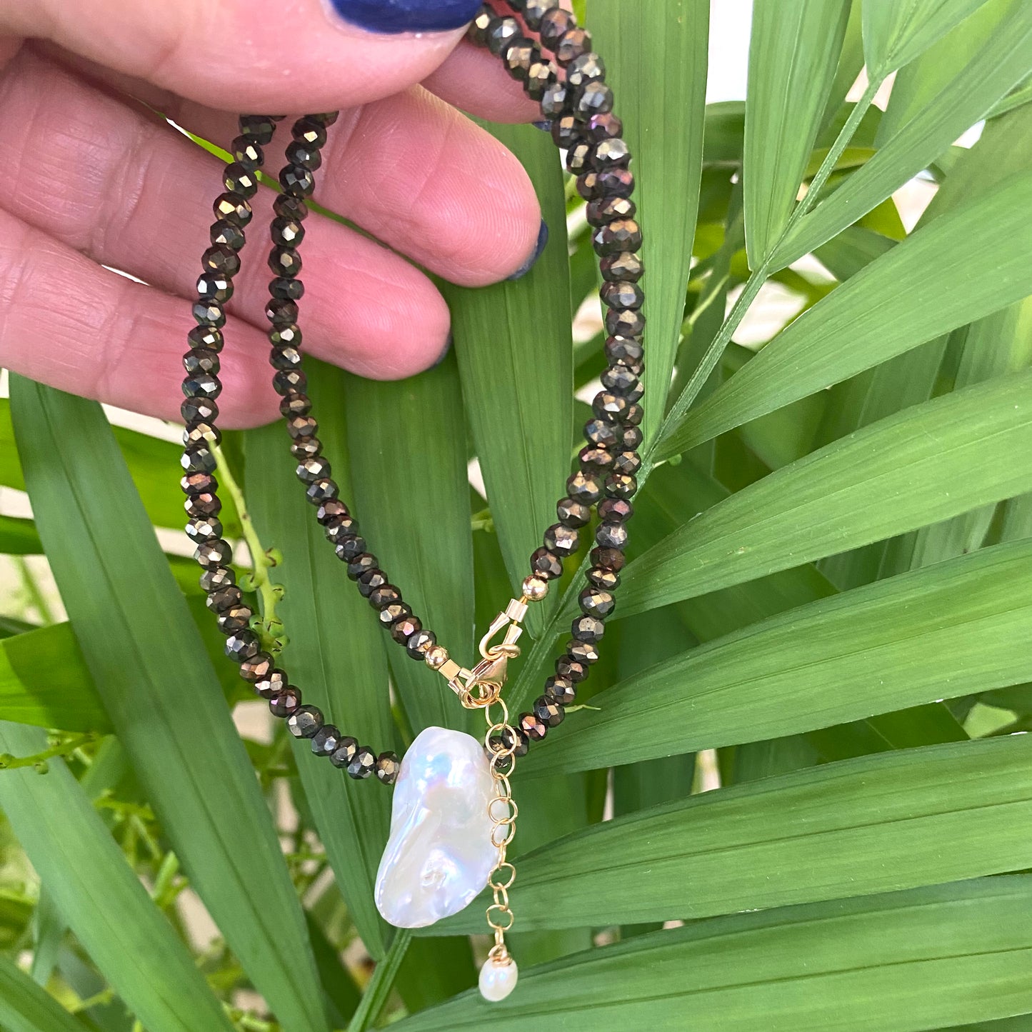 Pyrite pearl choker necklace with white keshi pearl showcased against lush green leaves.
