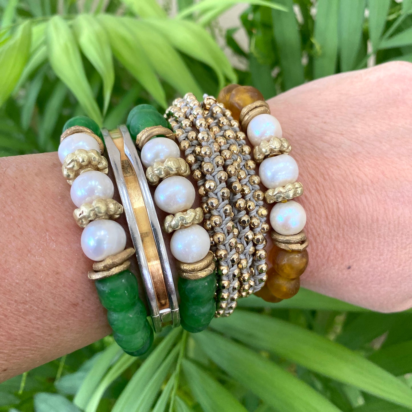 Pearl glass bracelet with green African recycled beads and gold accents on a wrist, surrounded by green foliage.