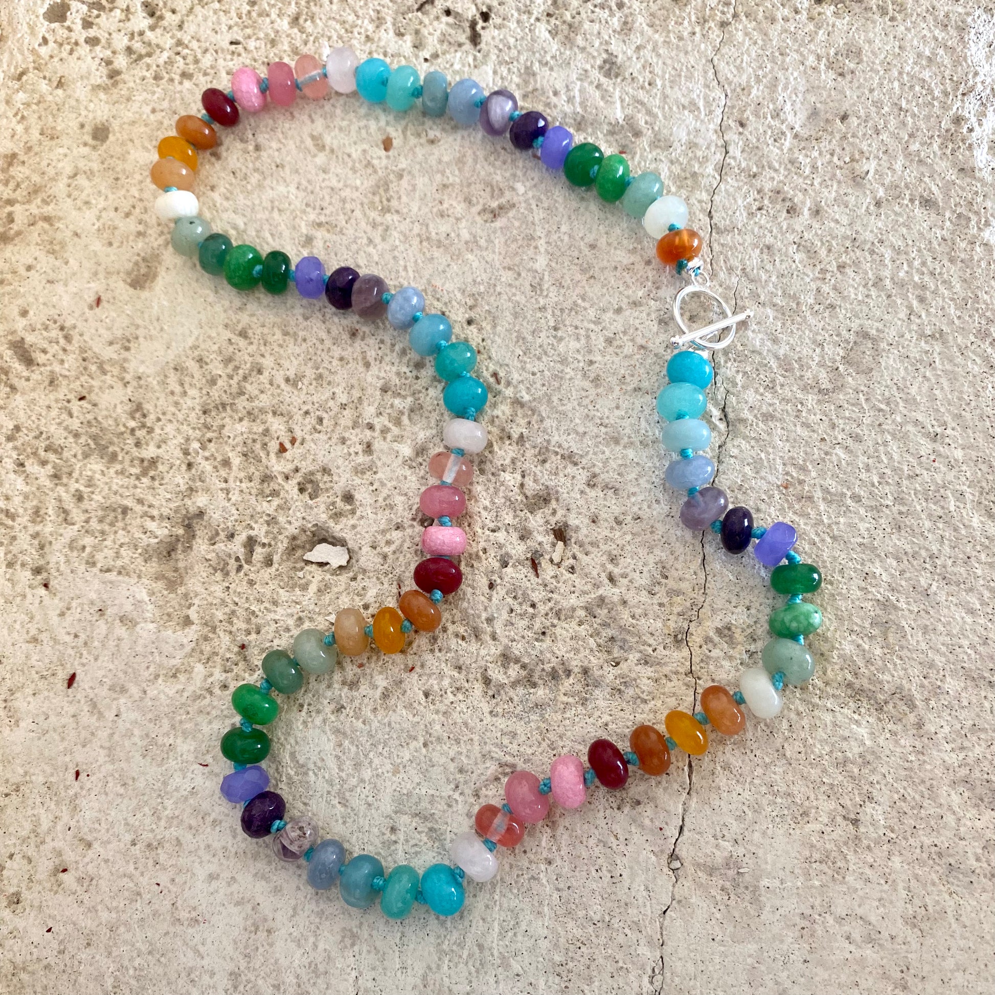 Rainbow candy necklace featuring vibrant gemstone rondelle beads and a silver clasp on a textured surface.
