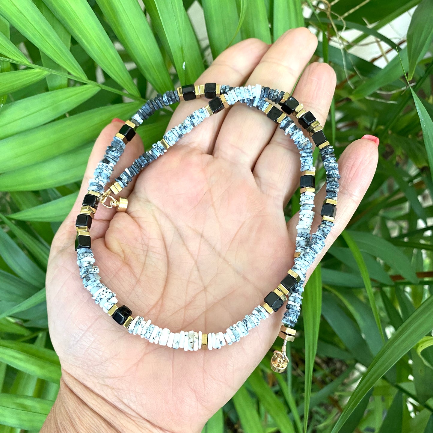 Dendritic opal necklace in hand on greenery, black and white opal heishi beads with black spinel accents