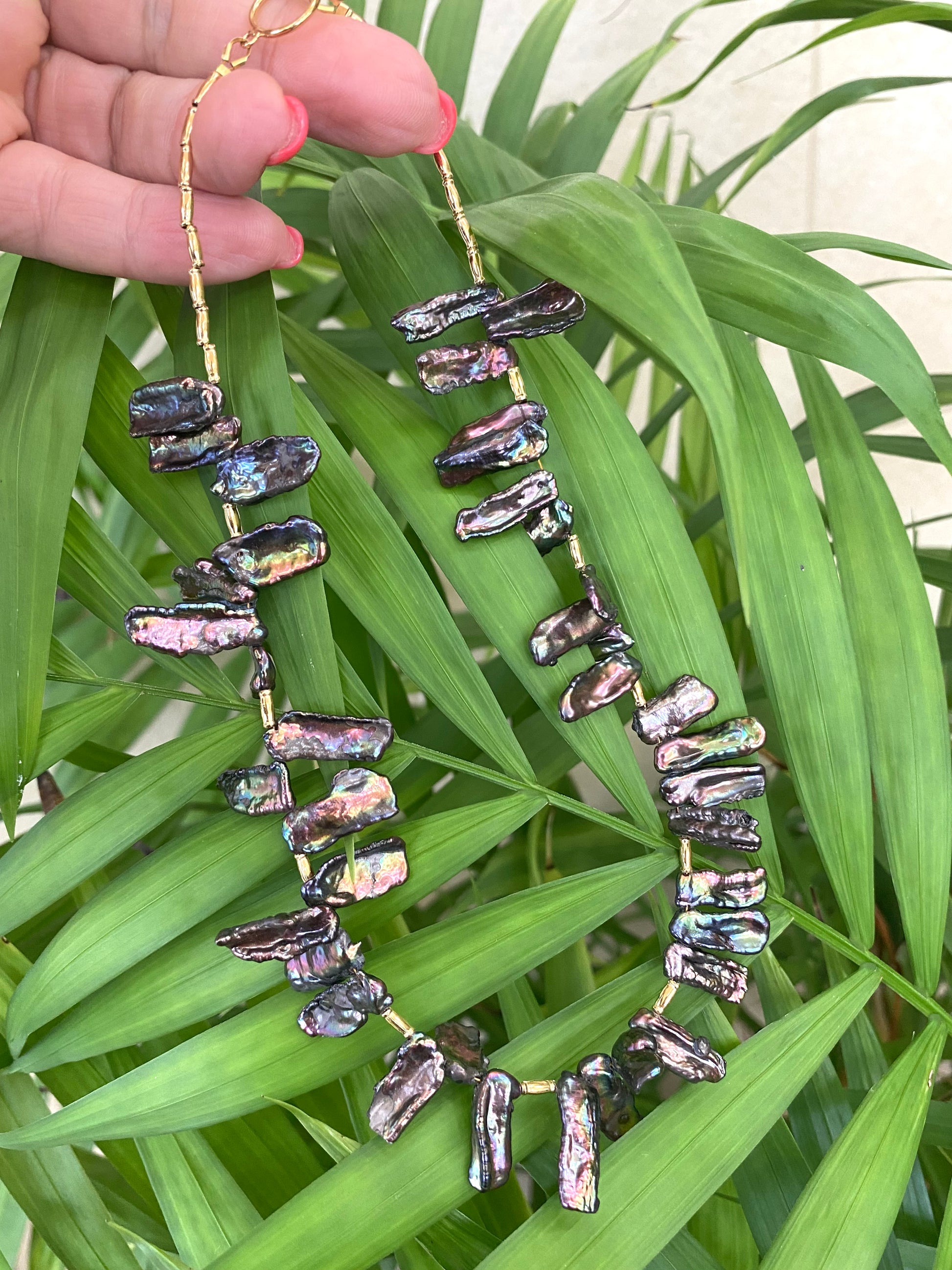 Black pearl choker necklace held up on green leaves, Biwa stick pearls with peacock iridescence