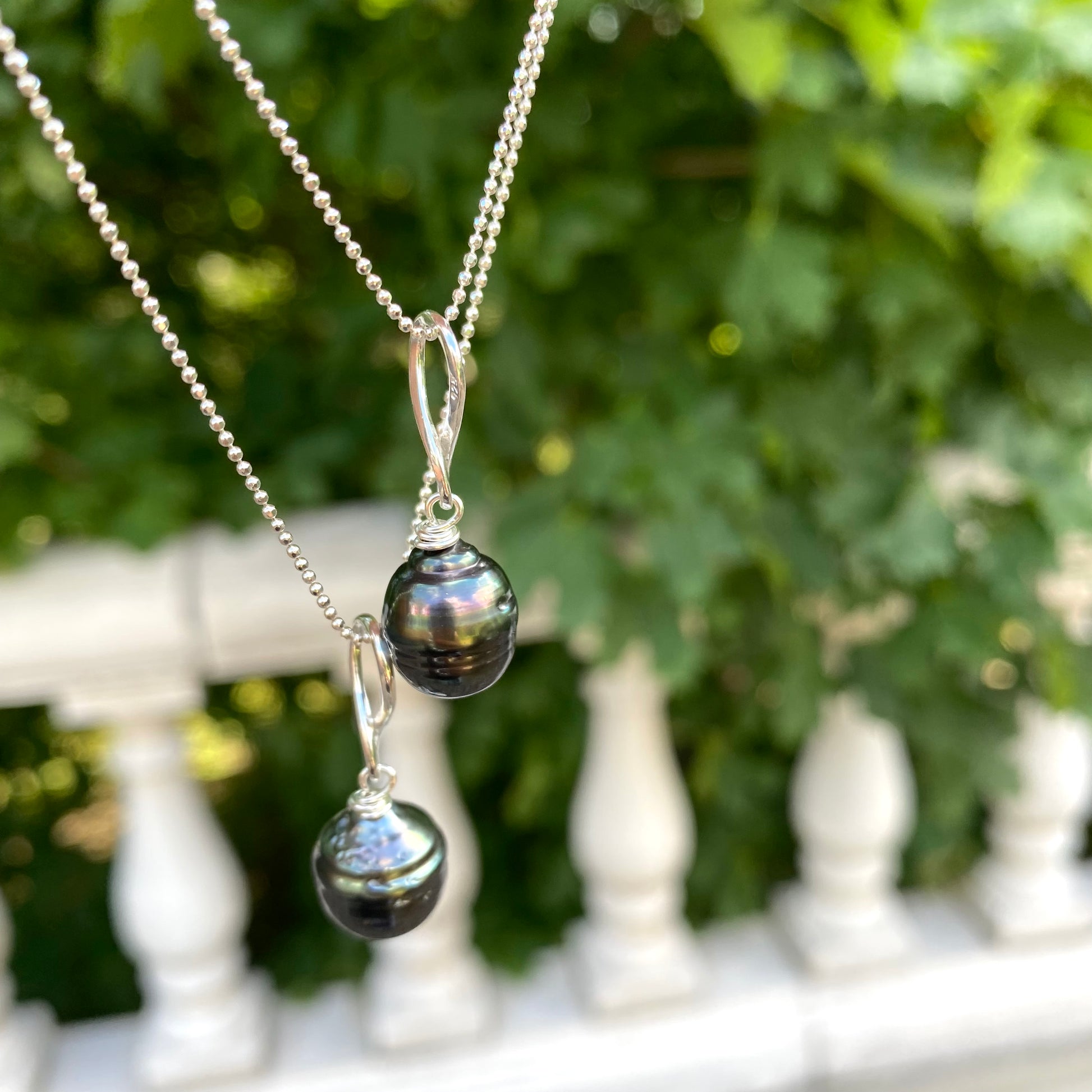 Tahitian teardrop pearl pendant necklace hanging outdoors, sterling silver ball chain and dark pearl pendant