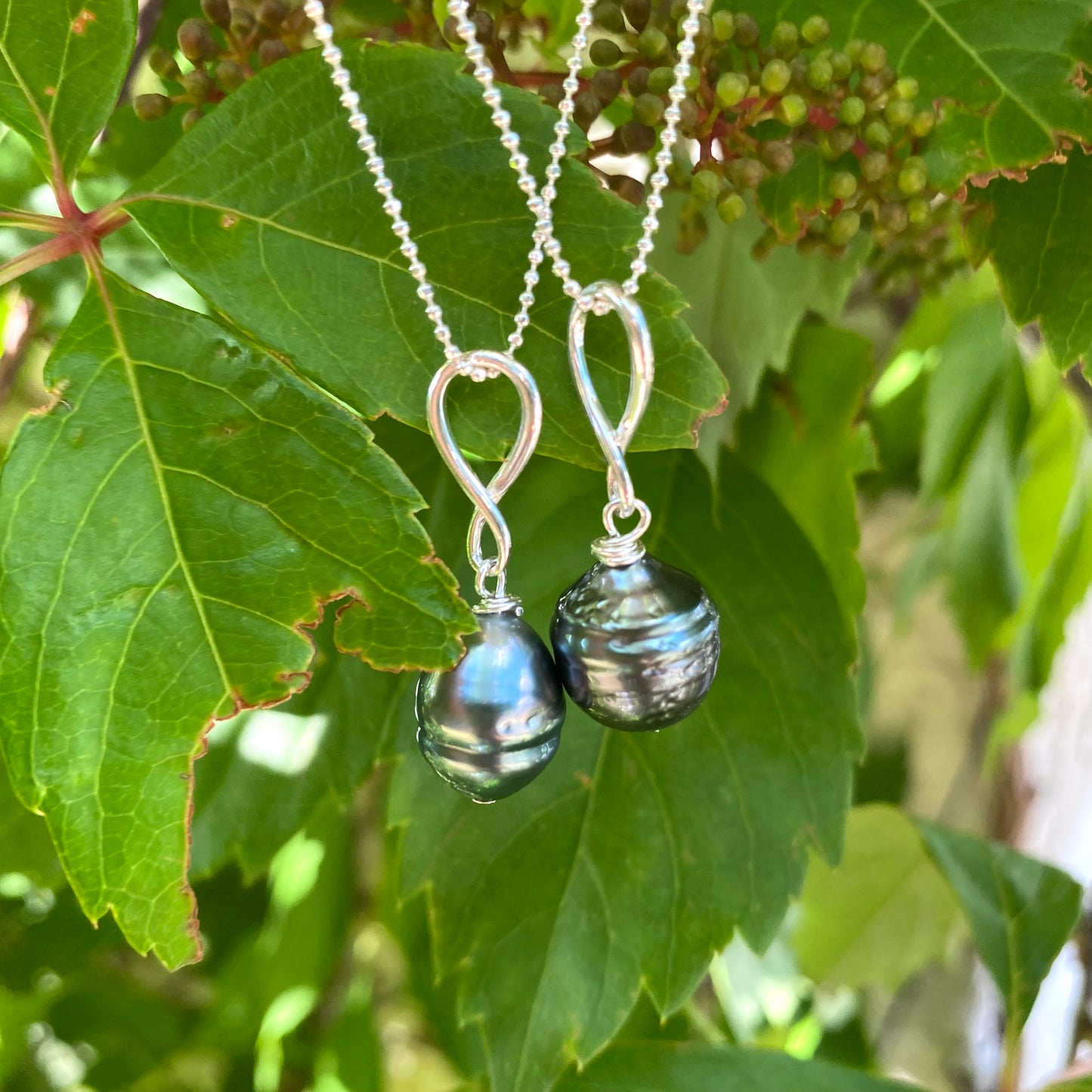 Tahitian teardrop pearl pendant necklace close-up on leaves, genuine Tahitian pearl pendant on silver chain