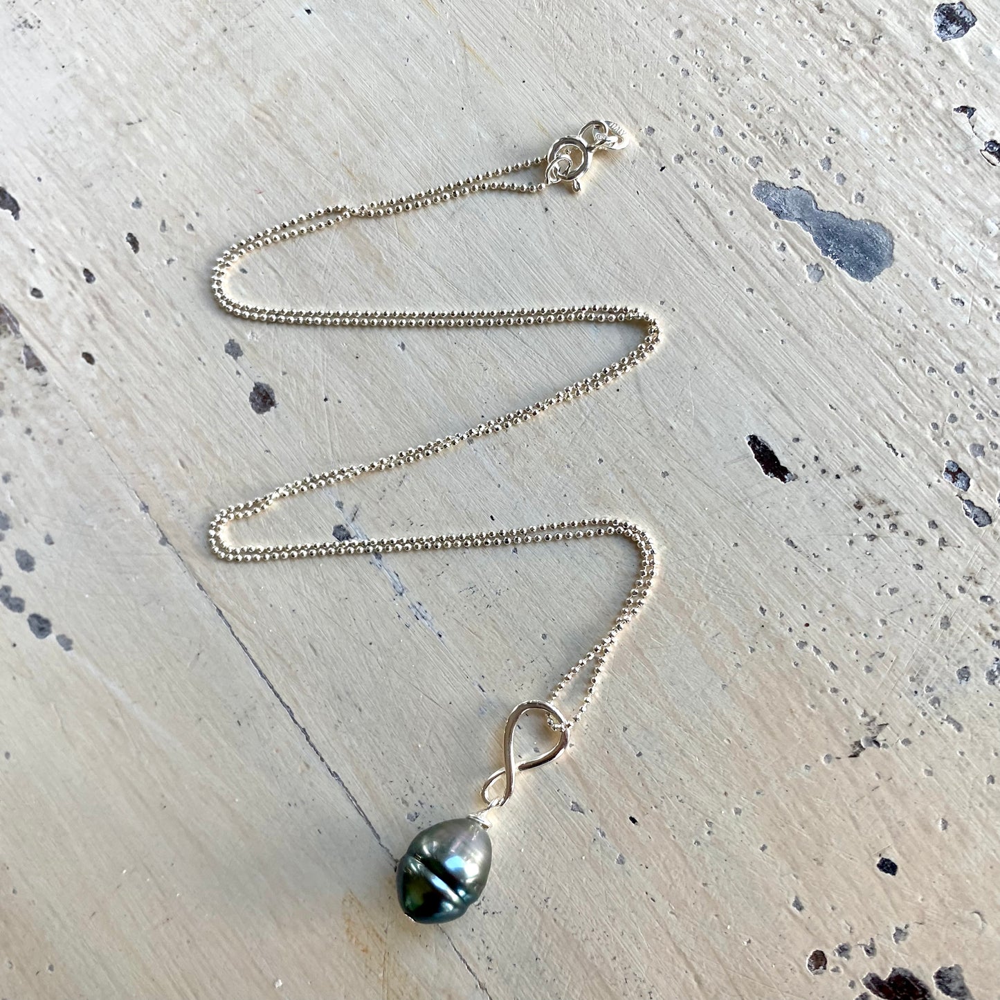 Tahitian teardrop pearl pendant necklace flat lay on tabletop, sterling silver ball chain detail