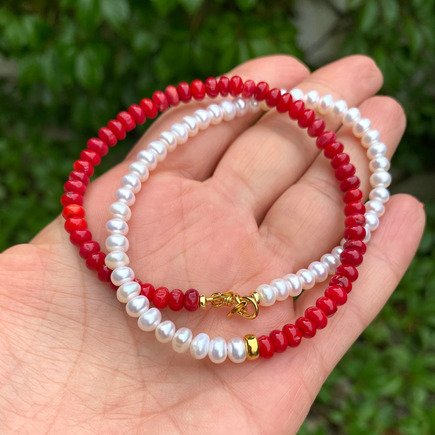 Half Coral Half Pearl Choker Necklace coiled in hand against greenery, red coral rondelles and freshwater button pearls