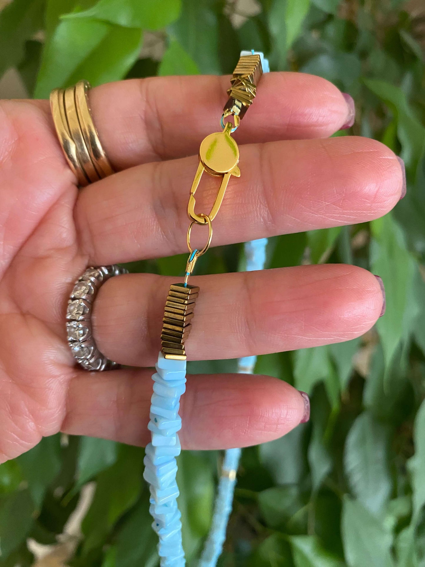 Close-up of a blue opal choker necklace being held, showcasing heishi square sky blue opal beads and a gold clasp.