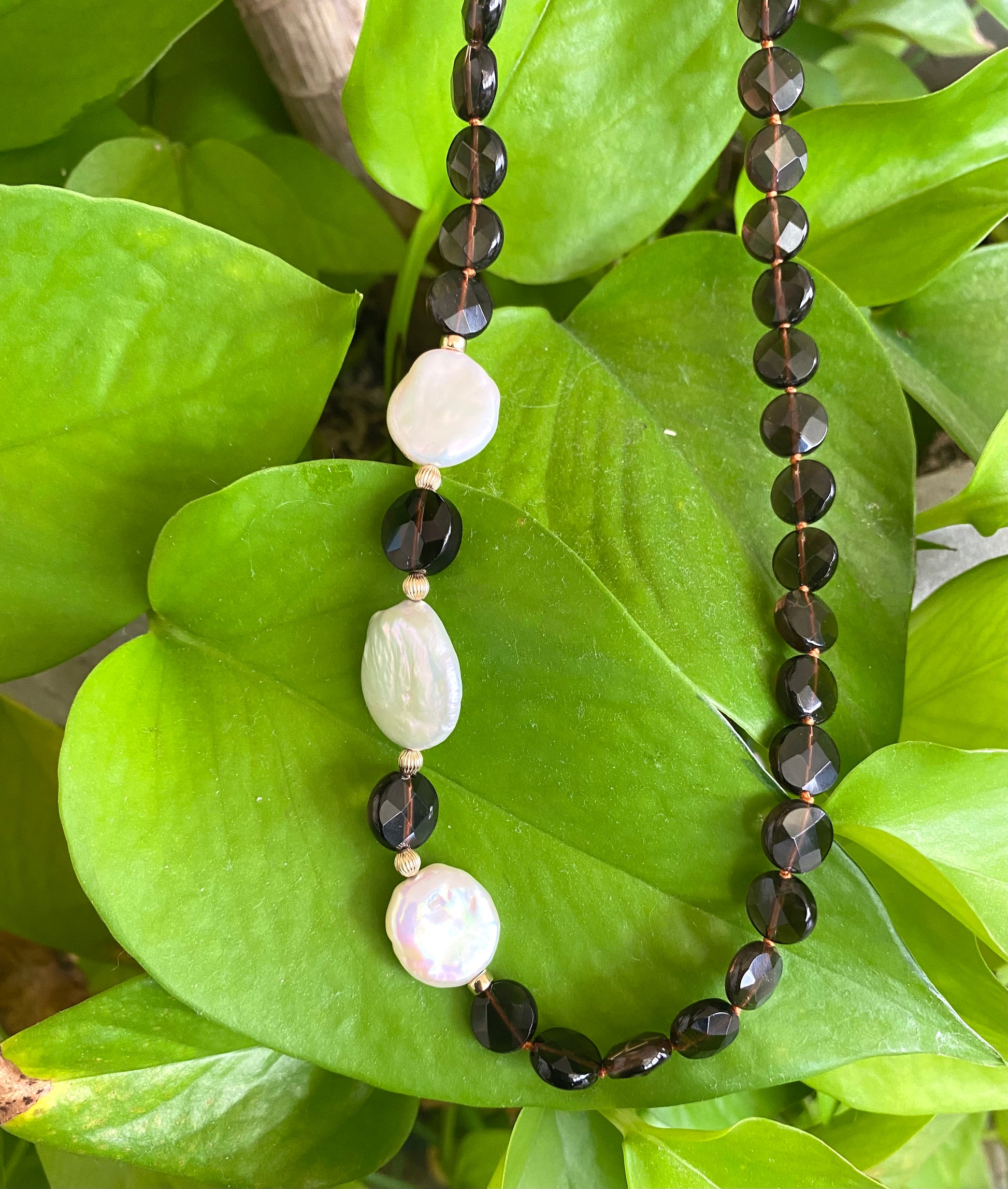 Smoky quartz pearl necklace with coin pearls showcasing rich earthy tones and elegant design on a green backdrop.