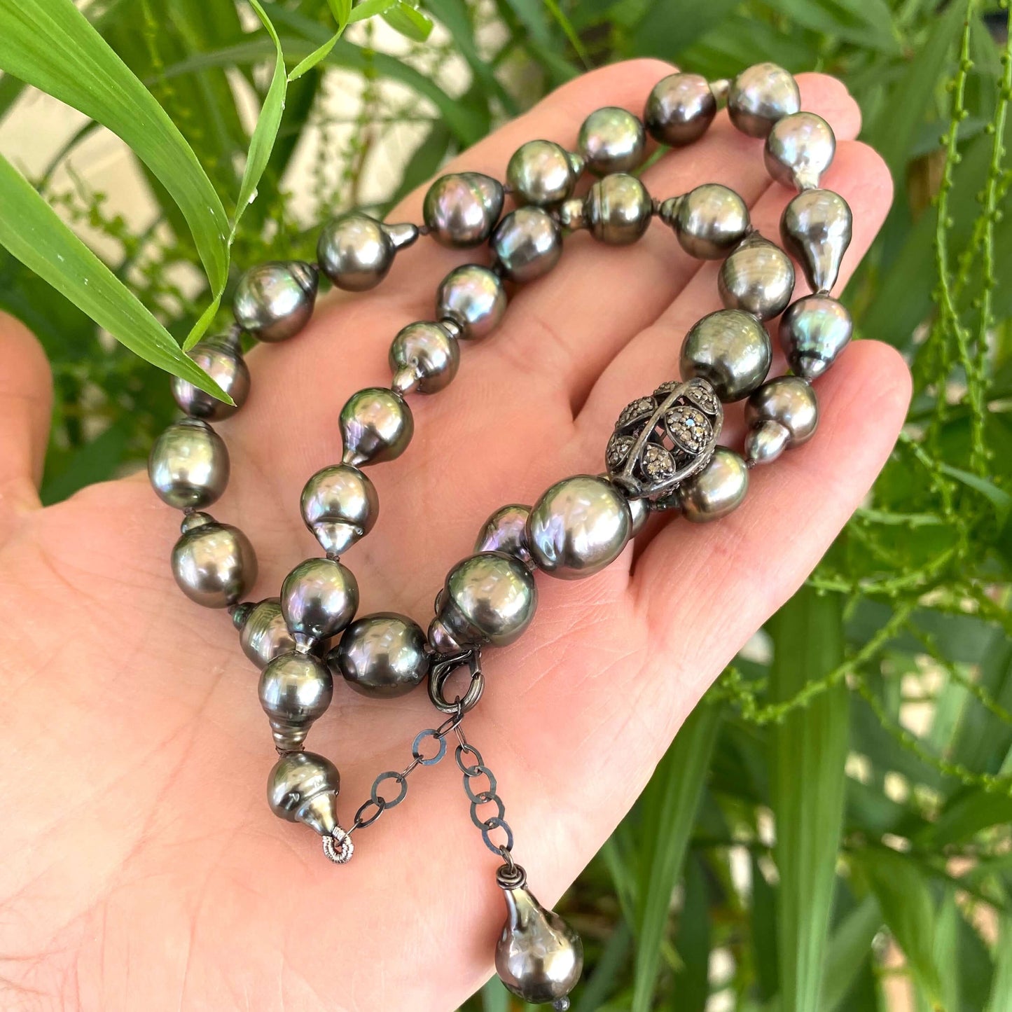 Tahitian baroque pearl necklace with champagne diamonds elegantly displayed in hand, showcasing deep grey tones and iridescence.
