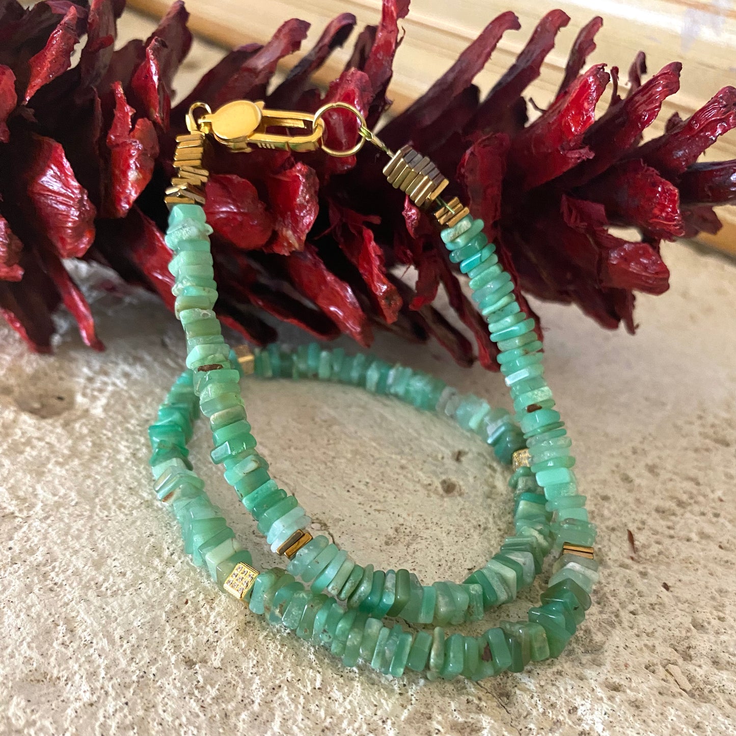 Chrysoprase choker necklace with green heishi beads and gold accents displayed on textured surface.