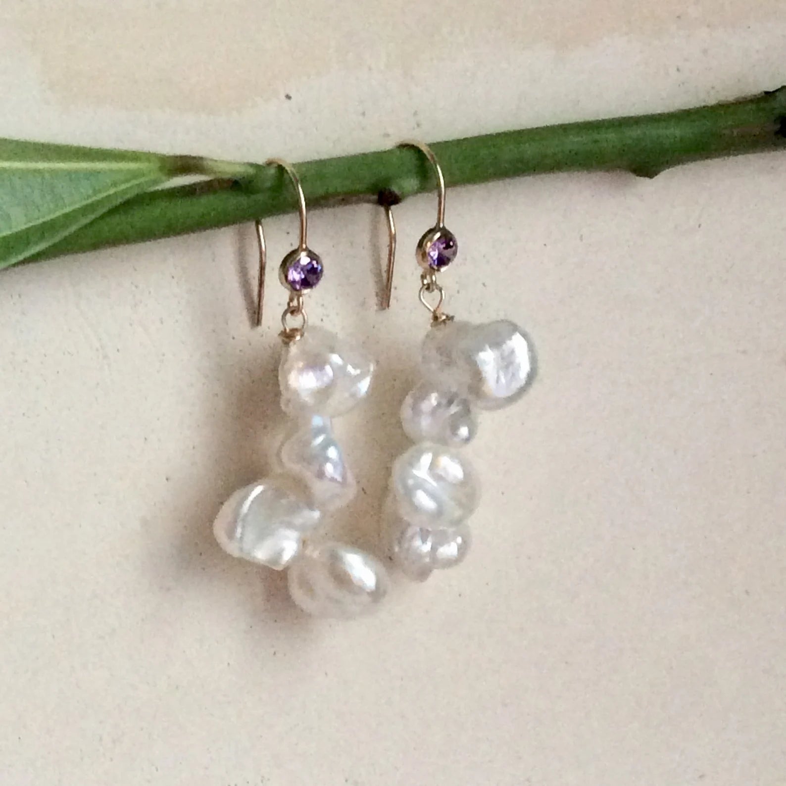 Keshi Pearl Drop Earrings – 14k Gold Filled with Purple CZ showcasing luminous keshi pearls on a leaf.