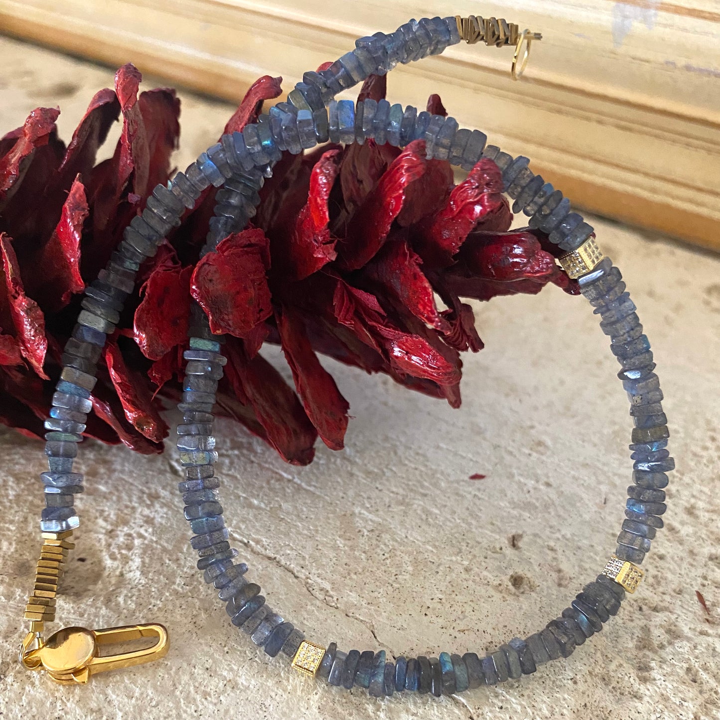 A labradorite choker necklace with hematite beads and gold vermeil details, displayed on a red, fabric-like surface.